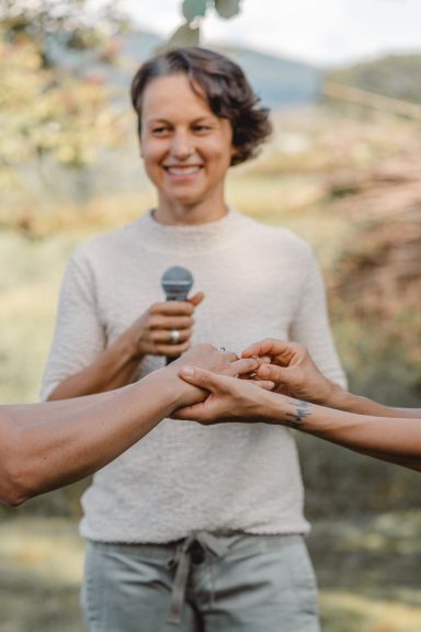 Eine lächelnde Person mit einem Mikrofon steht vor anderen, die Hände halten.