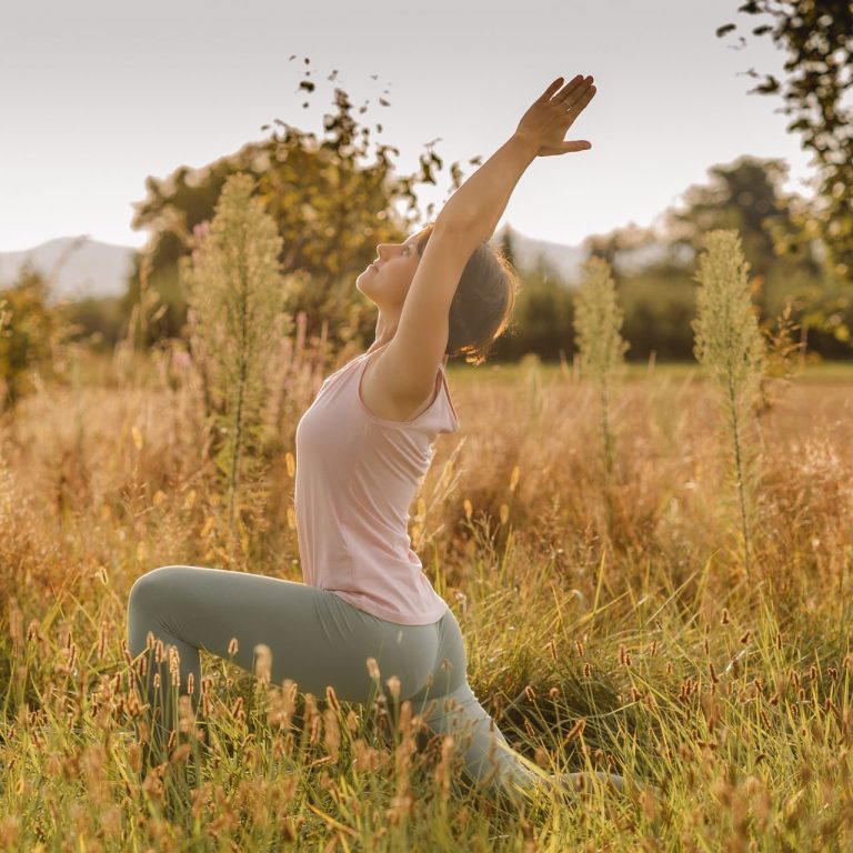 Eine Person übt Yoga in einer Wiese mit sanften Hügeln im Hintergrund.